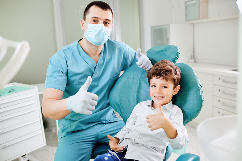 Child and dentist giving thumbs up while smiling