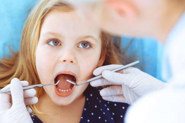 A little girl has her mouth open while a dentist inspects her teeth