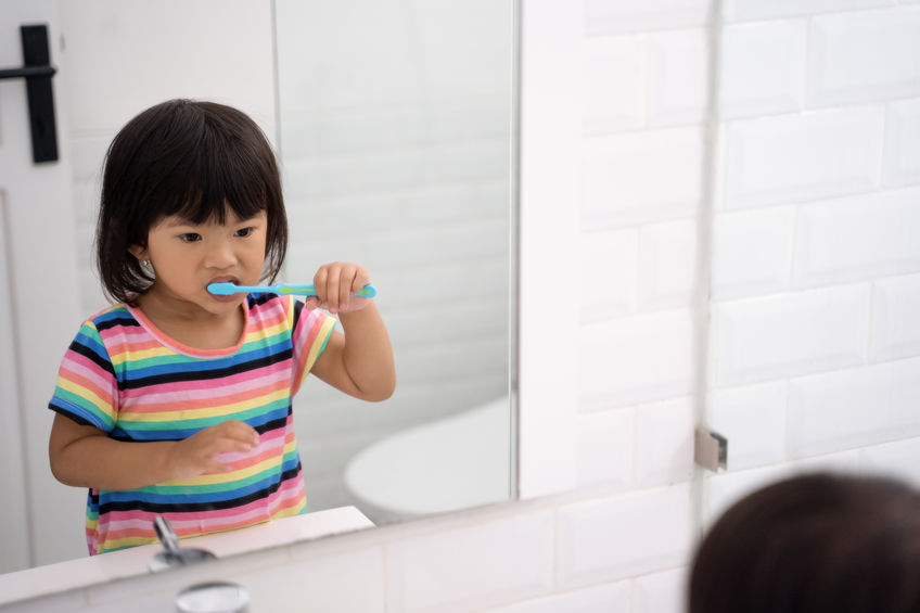A young girl wearing a rainbow shirt brushes her teeth