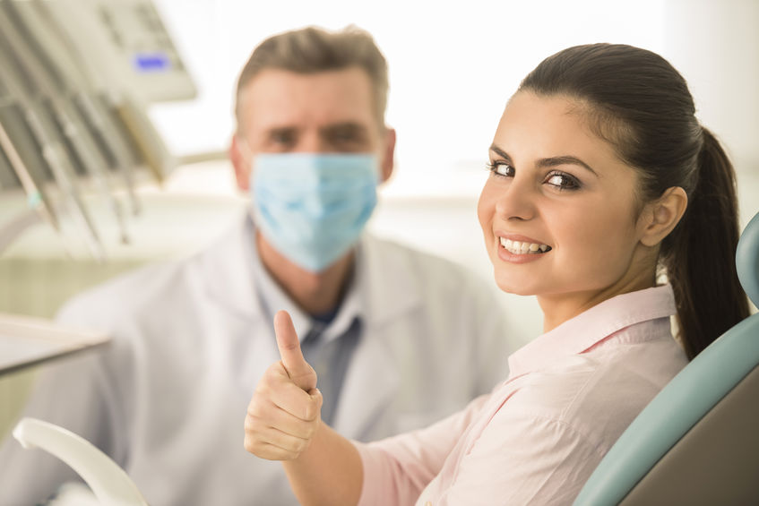 A woman at the dentist's office gives a thumbs up with a dentist in the background